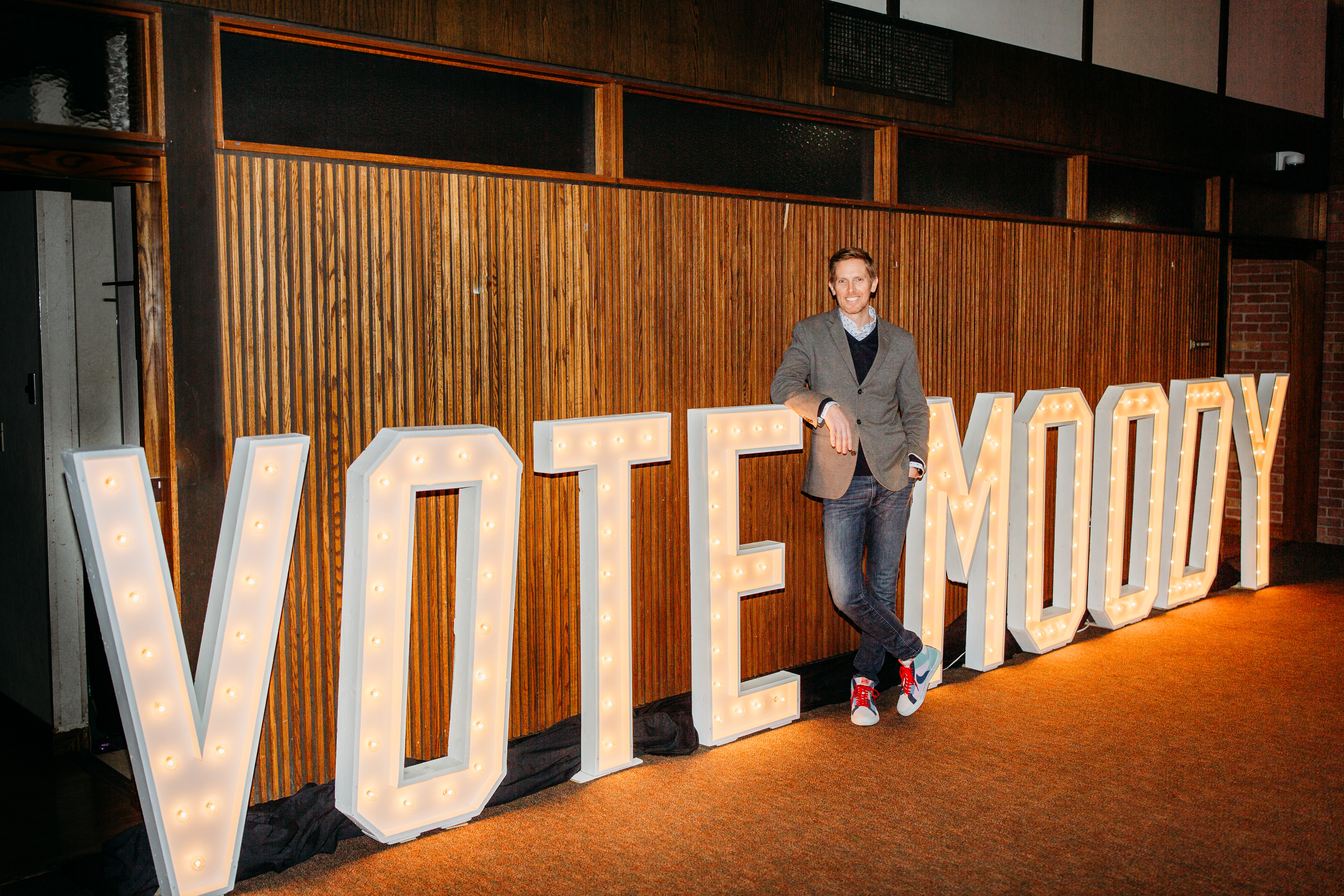 Craig Moody stands in front of tall letters that read VOTE MOODY
